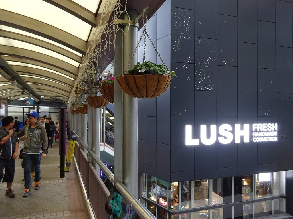 지붕이 있는 보행로 옆 러쉬 매장의 검은 외벽과 흰색 LUSH 간판